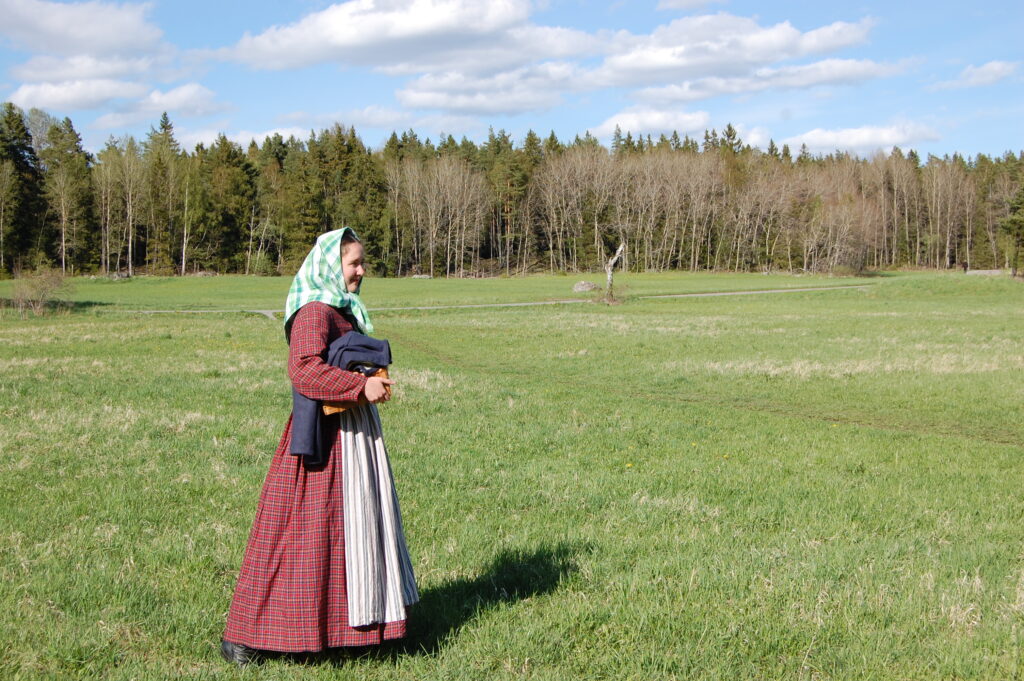 Linnea Dunér i rödrutig 1800-talsklänning, förkläde och sjalett